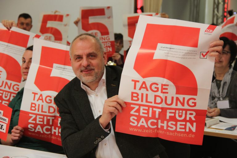 Man sieht Rico Gebhardt und andere Delegierte, die ein Plakat hochhalten auf dem steht "5 Tage Bildung. Zeit für Sachsen"