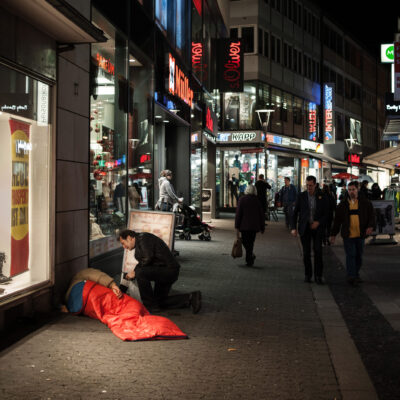 Gerhard Trabert spricht mit einem Menschen im Schlafsack in einer Innenstadt